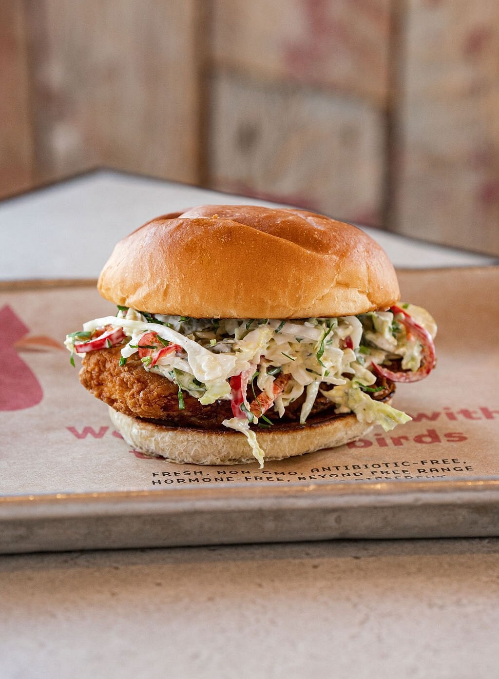 A fried chicken sandwich with coleslaw in a toasted bun sits on a tray lined with brown paper.