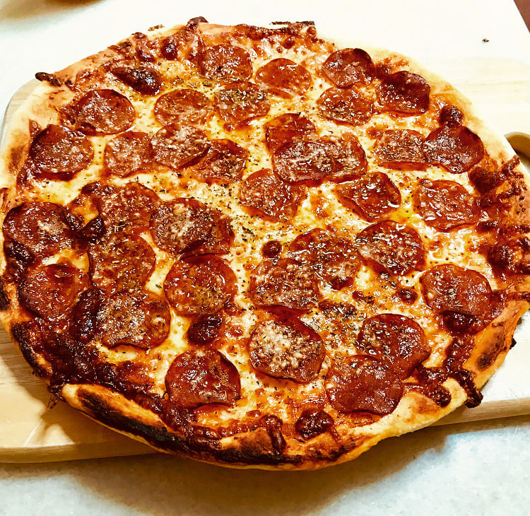 A freshly baked pepperoni pizza on a wooden board, topped with melted cheese, crispy pepperoni slices, and a sprinkle of herbs.