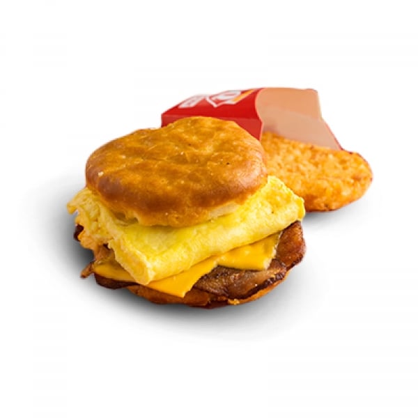 A breakfast sandwich with egg, cheese, and sausage on a biscuit, served with a golden hash brown in a red wrapper, on a white background.