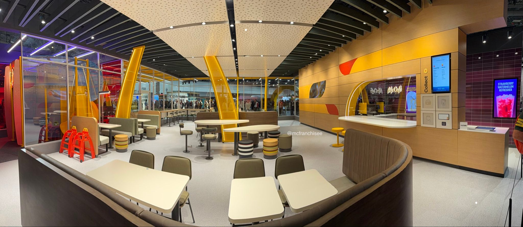 A modern fast-food restaurant interior with colorful seating, unique yellow partitions, digital kiosks, and playful decor. People can be seen outside through large glass windows.