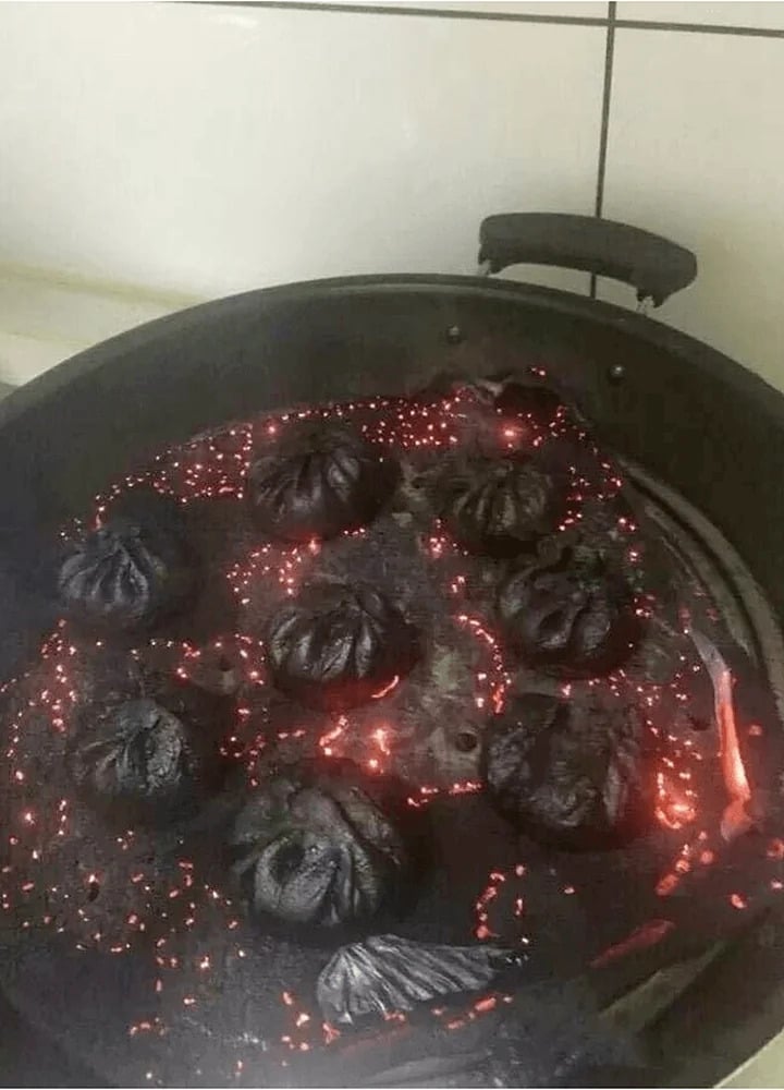 A frying pan with severely burnt dumplings, glowing red embers scattered among the blackened food, suggesting they were overcooked or left on the stove for too long.