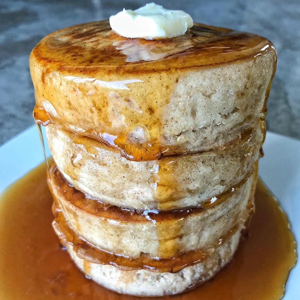 Three thick homemade pancakes stacked on a white plate, topped with a pat of butter and generously drizzled with syrup.