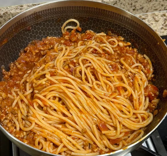 Spaghetti mixed with ground meat and tomato sauce in a large pan on a stovetop, ready to be served.