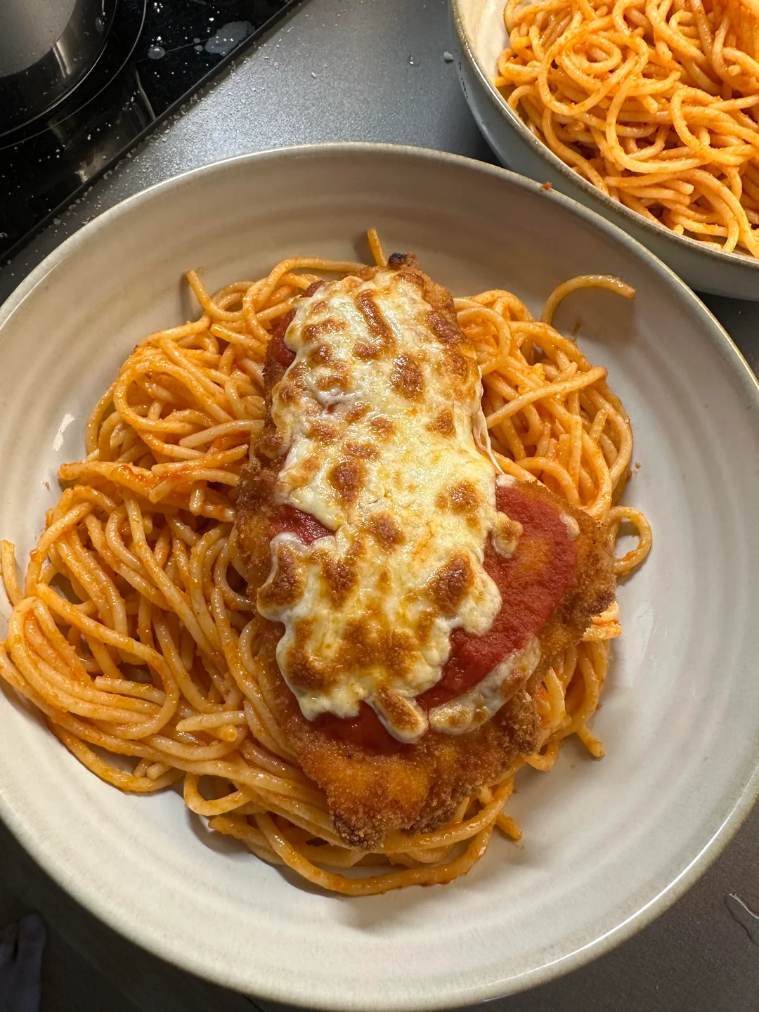 A plate of spaghetti with tomato sauce is topped with a breaded chicken cutlet covered in melted cheese and sauce, resembling chicken parmesan.