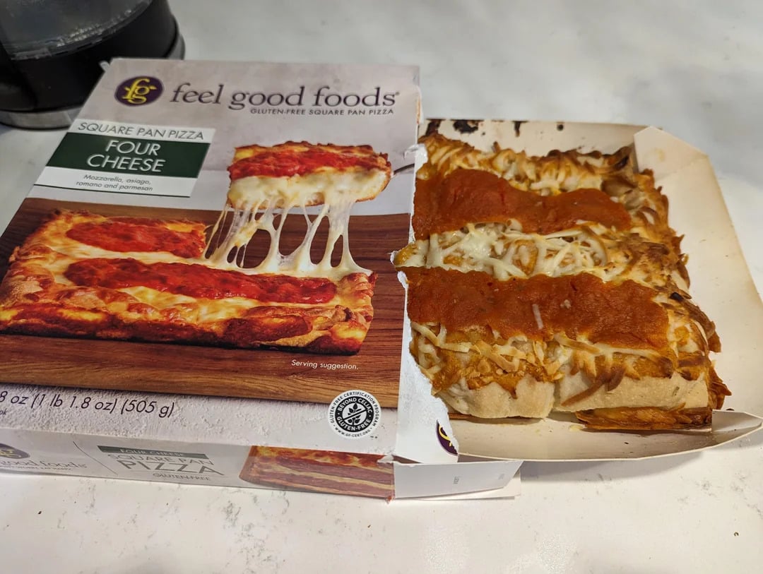 Opened box of "feel good foods" Four Cheese Square Pan Pizza next to the cooked pizza, showing melted cheese and sauce, on a light countertop. The pizza closely resembles the picture on the box.