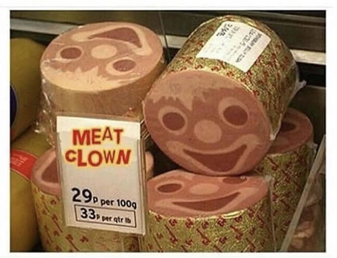 Sliced deli meat with a clown face pattern shown on each slice. A sign in front reads "MEAT CLOWN" with the price per 100g and per quarter pound listed below.