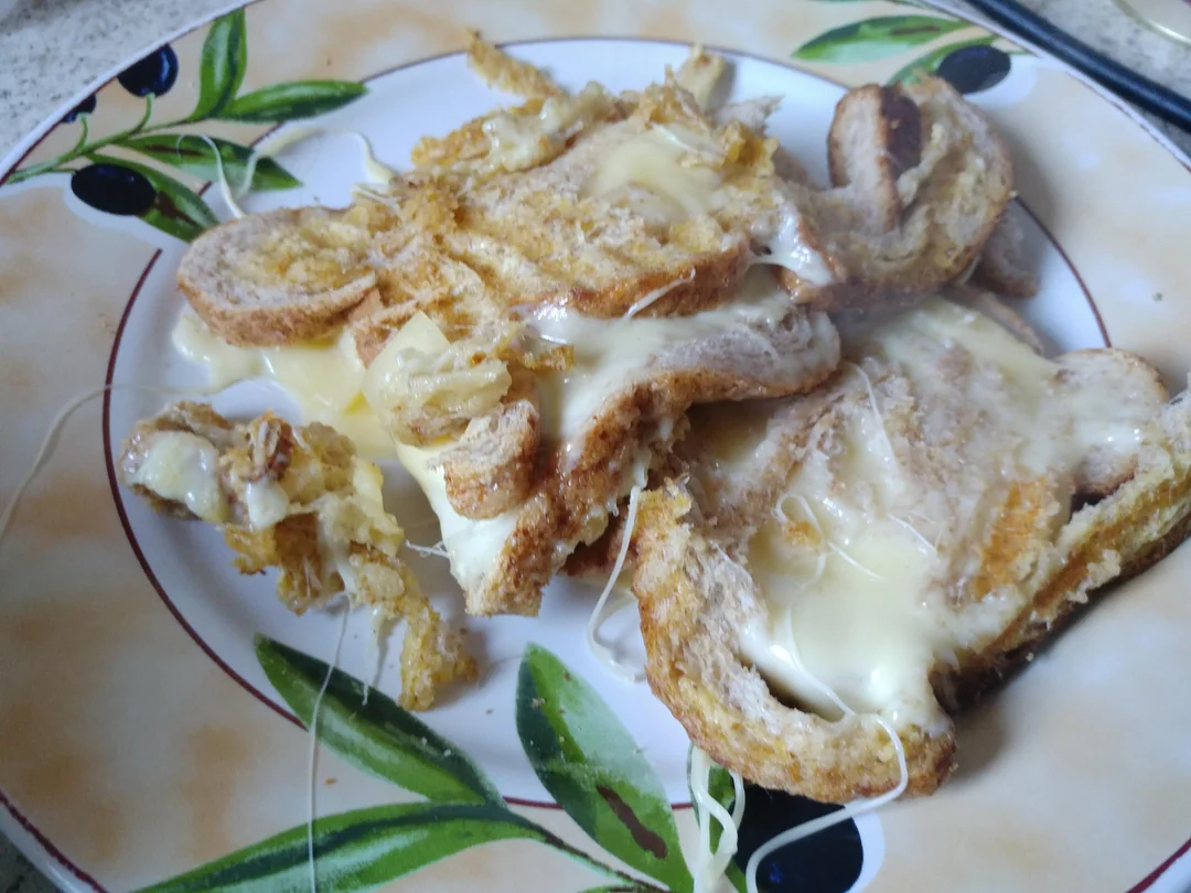 Melted cheese on toasted bread slices sits on a decorative plate with olive and leaf patterns.