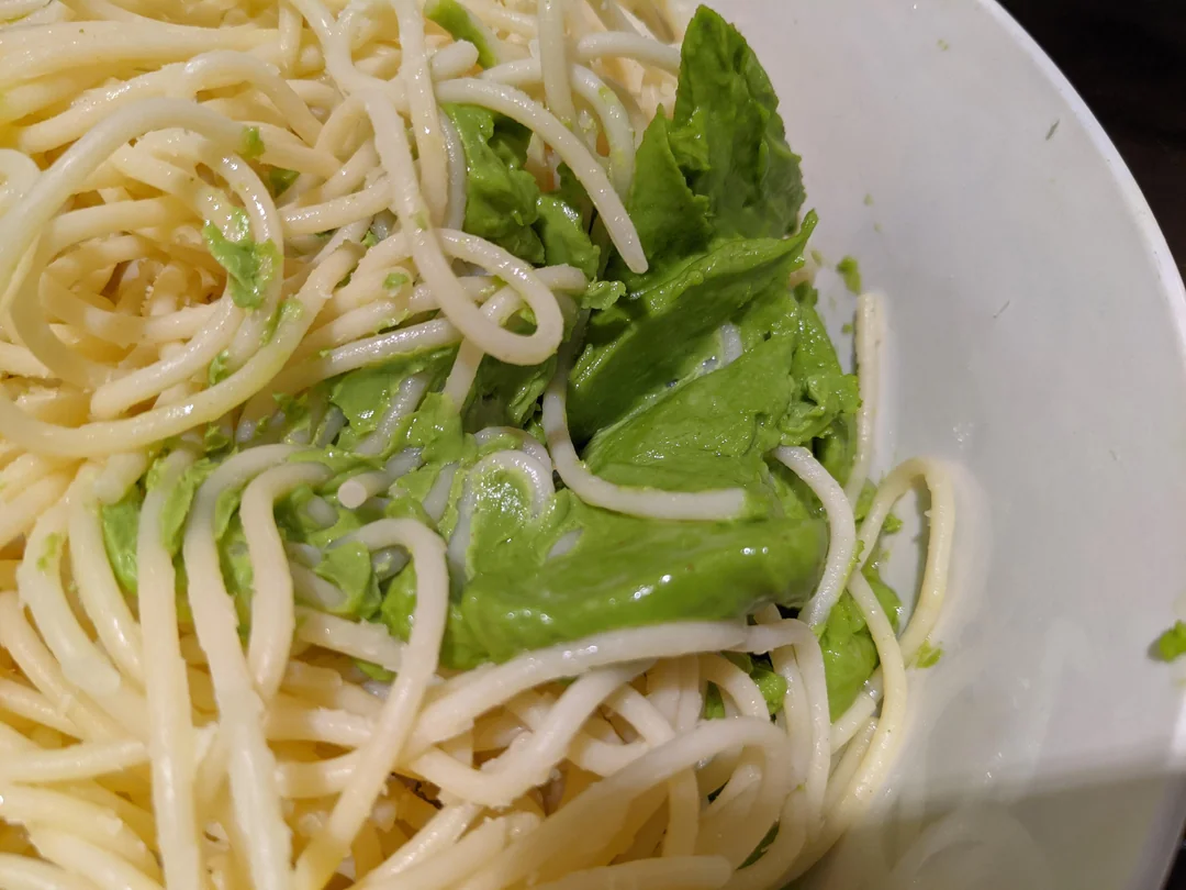 A close-up of cooked spaghetti noodles in a white bowl, mixed with a few green lettuce leaves.