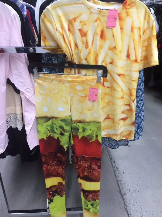 A clothing set with a T-shirt printed with French fries and leggings printed with a hamburger, hanging on a clothing rack in a store.