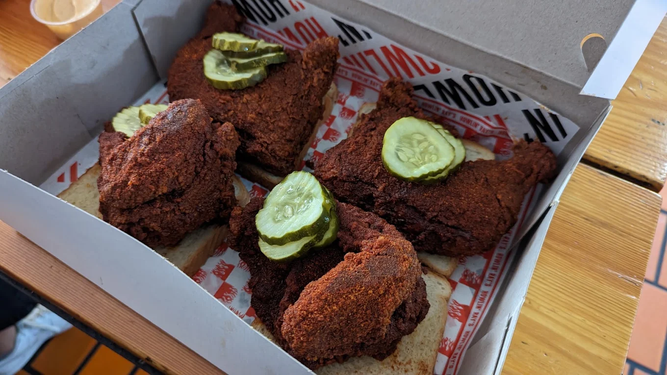 Four pieces of spicy fried chicken topped with pickle slices, served on white bread in a takeout box.