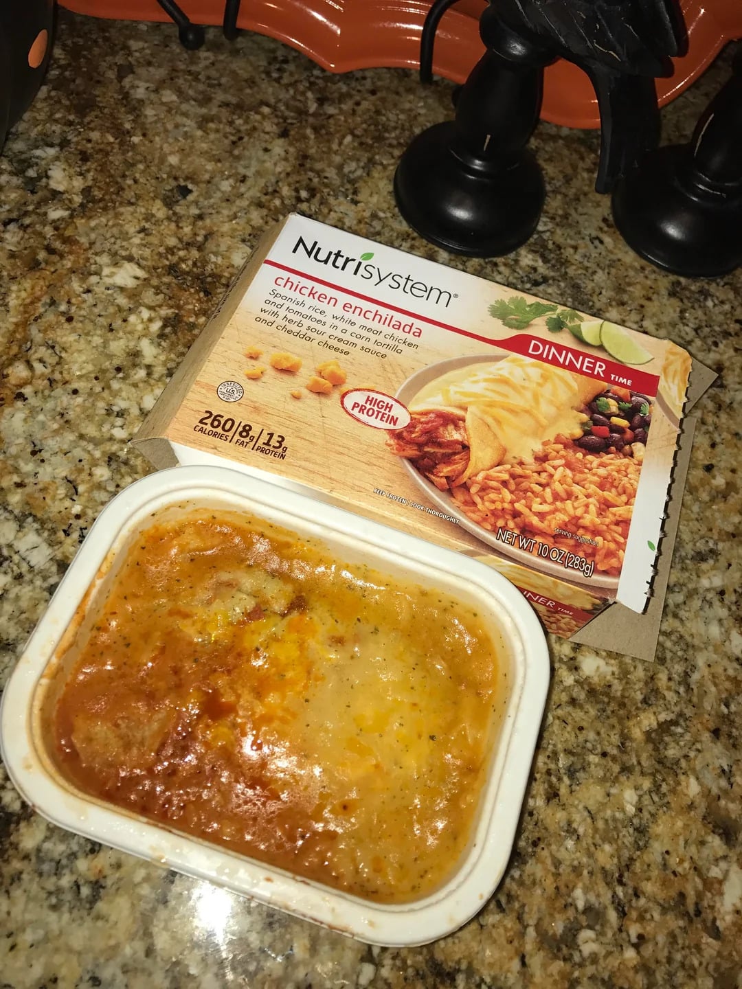 Nutrisystem chicken enchilada meal shown on a granite countertop, with the prepared entree in a plastic tray in front of its packaging.