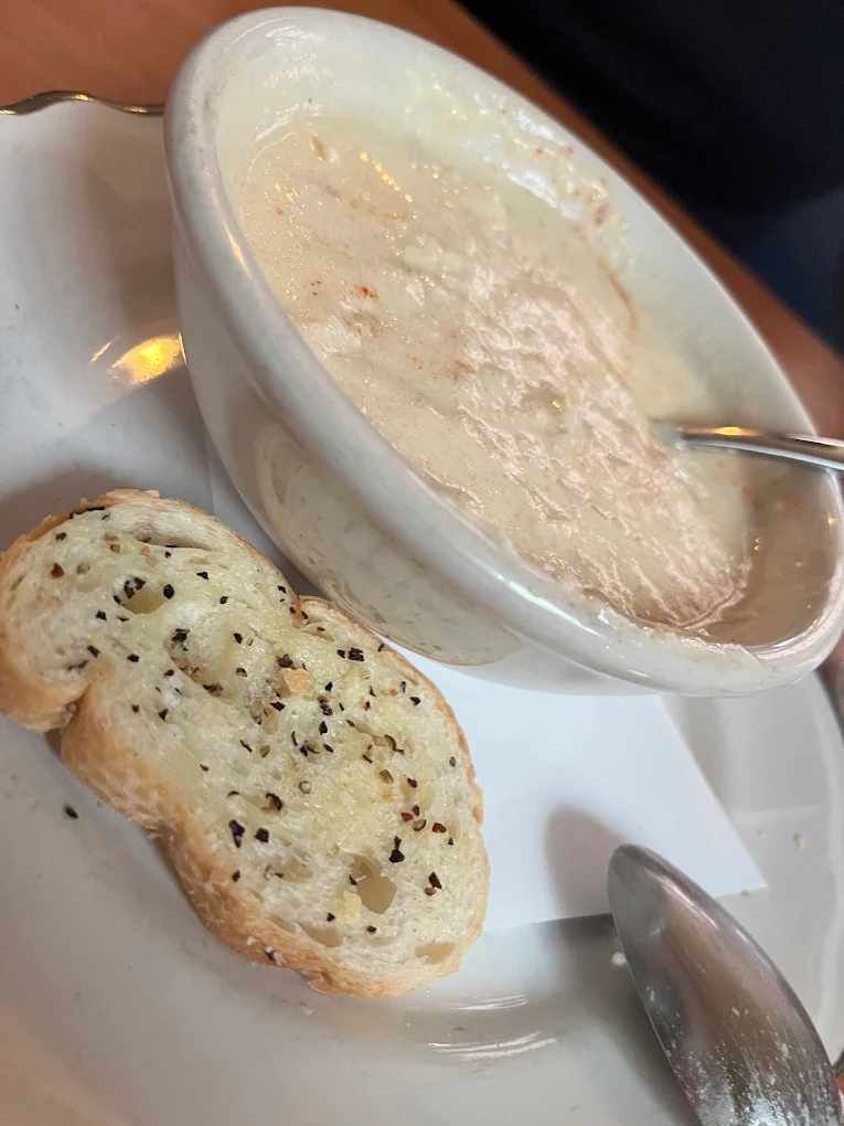 A bowl of creamy soup with a spoon, served on a white plate with two slices of toasted bread seasoned with black pepper.