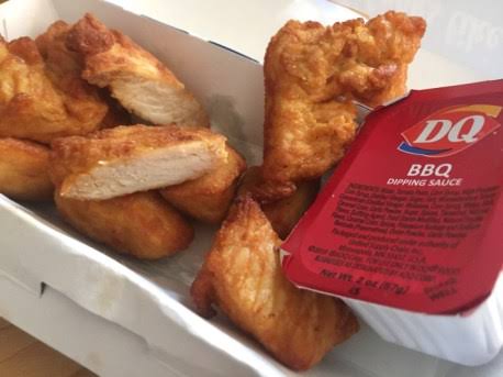 Six pieces of golden brown chicken strips in a white tray, served with a Dairy Queen BBQ dipping sauce container on the side.