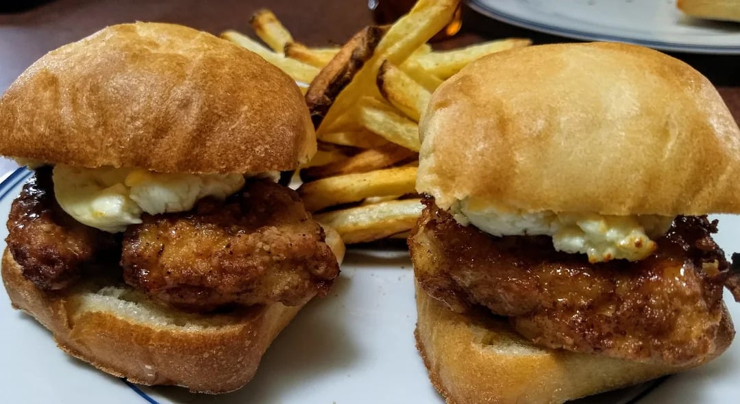 Two fried chicken sliders with a spread of white sauce on buns, served with a side of golden French fries on a white plate.