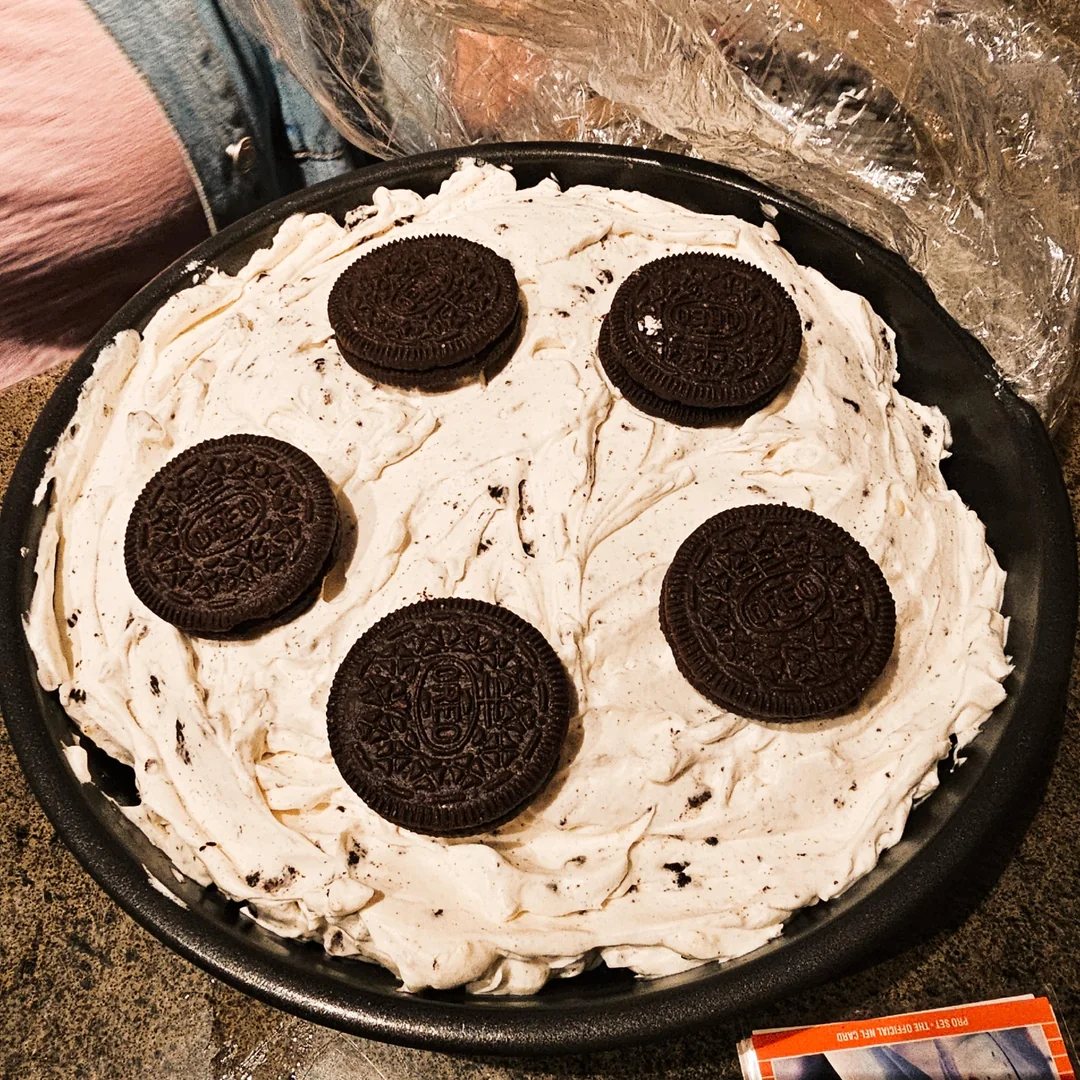 A round pie topped with cream mixed with cookie pieces, this delightful treat is one of the best homemade desserts, decorated with five whole chocolate sandwich cookies arranged on top.