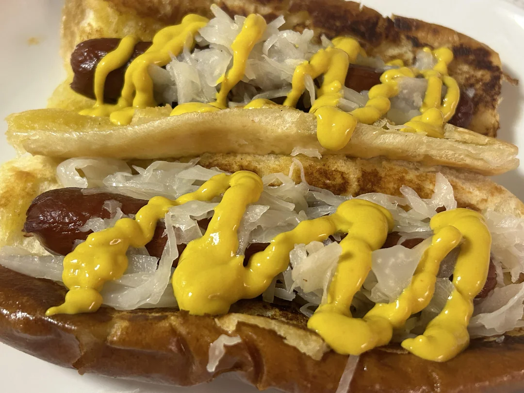 Two hot dogs in buns topped with sauerkraut and drizzled with yellow mustard, served on a white plate.