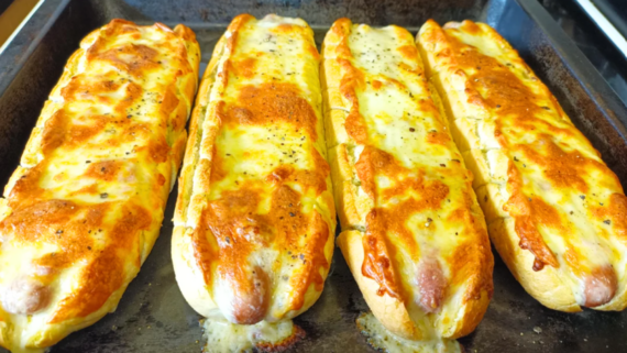 Four baked cheese-stuffed baguettes with melted golden cheese and herbs are lined up on a baking tray, resembling the mouthwatering appeal often seen in irresistible hot dog photos.