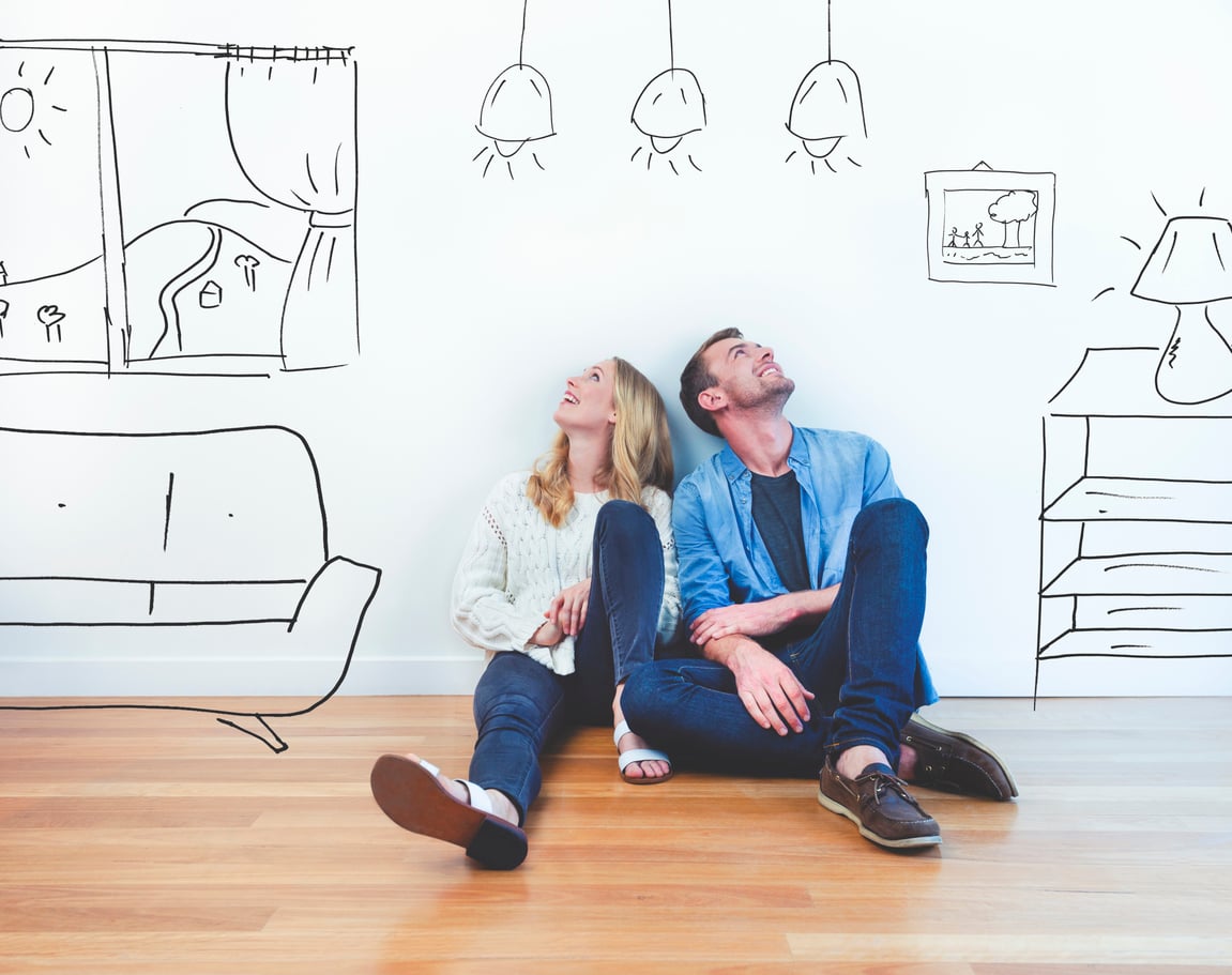 A woman and man sit on a wooden floor, leaning against a white wall decorated with black line drawings of furniture, windows, and lampsāperhaps imagining changes as they consider which home features homeowners no longer wantālooking up and smiling.