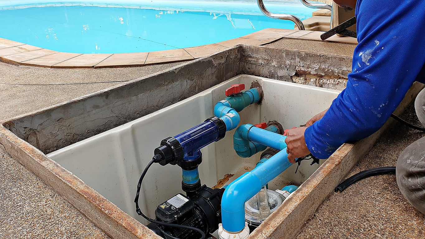 A person in a blue shirt works on blue PVC pipes and a pump in a maintenance compartment near a swimming poolāone of those home features homeowners no longer want.