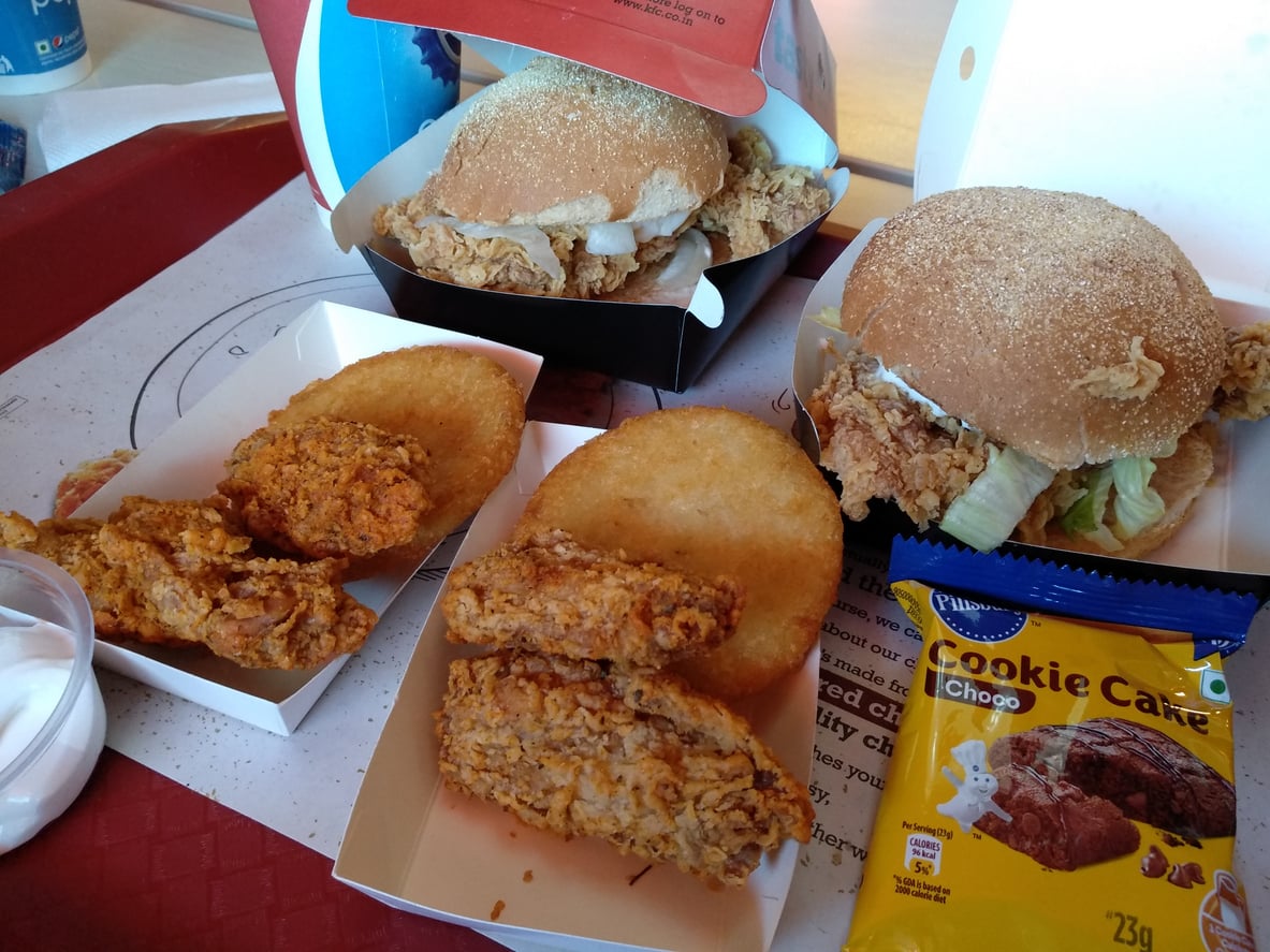 Two fried chicken sandwiches, fried chicken pieces, hash browns, a cookie cake packet, and a small container of sauce—served on a red tray—offer a taste reminiscent of regional fast-food chains.