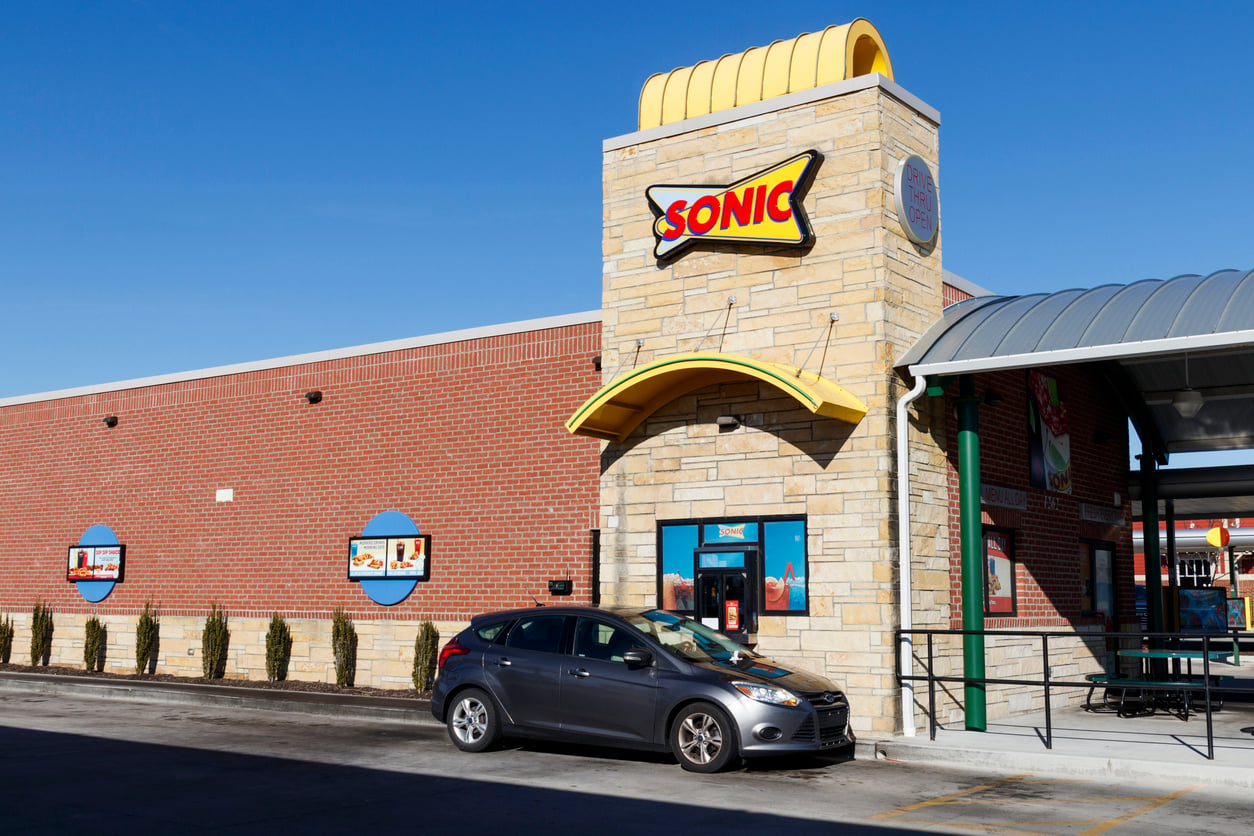 A gray car is parked in front of a Sonic fast food restaurant with a brick exterior and a tall sign featuring the Sonic logo under a clear blue sky. Worst fast-food breakfast