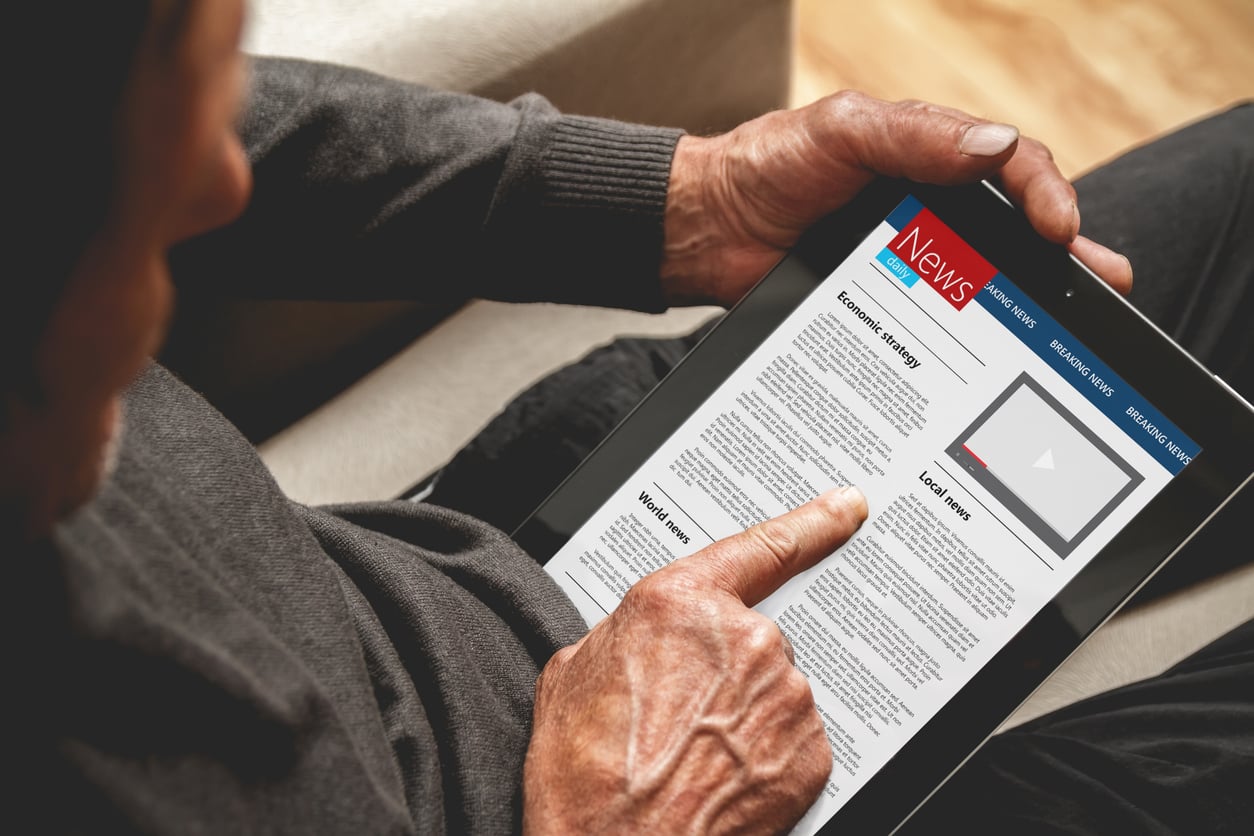 A person holding a tablet and reading an online news article, with headlines and a video section visible on the device’s screen—a modern contrast to life before smartphones, when accessing news was far less immediate.