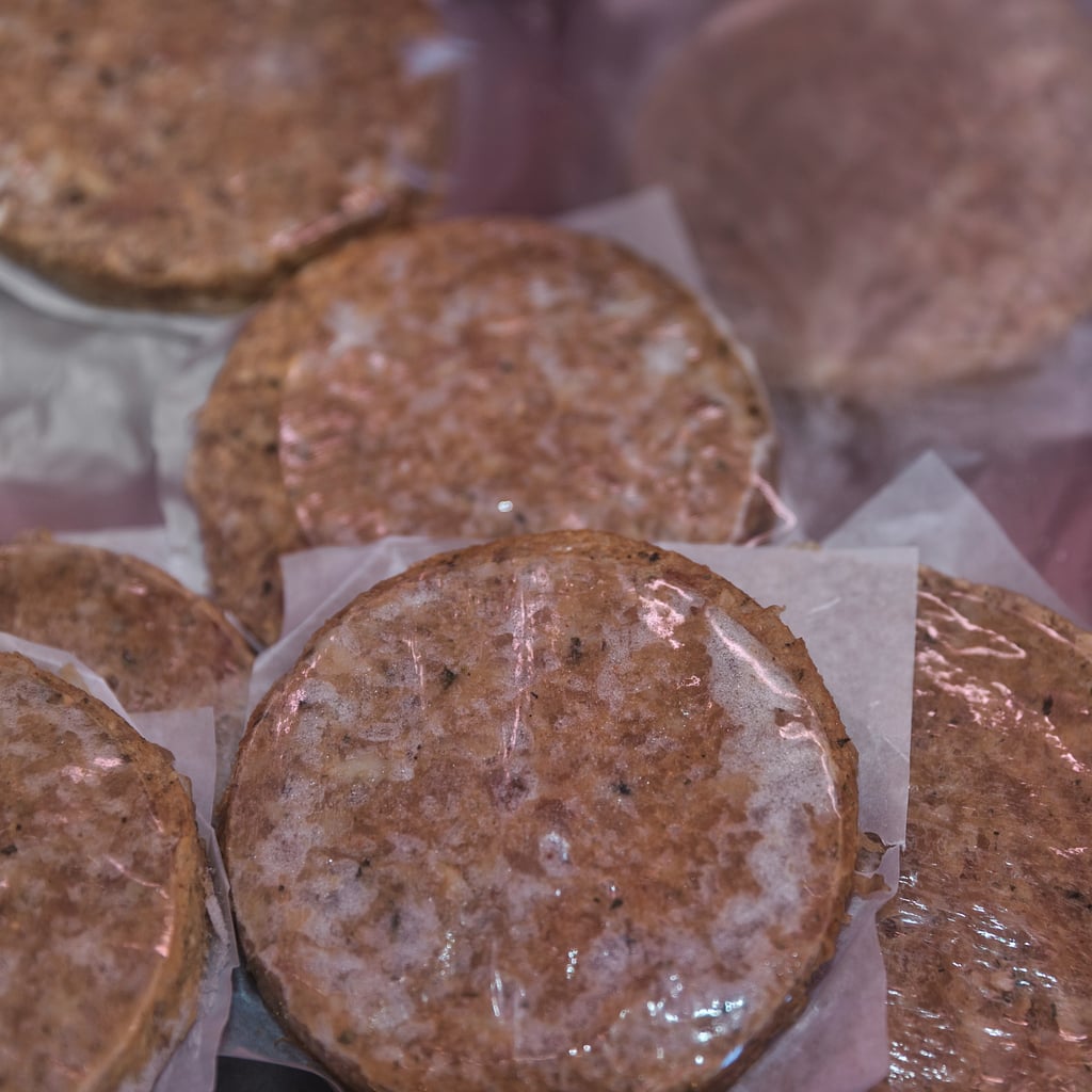 Several frozen hamburger patties are stacked with wax paper between each patty, ready for cooking or storage.