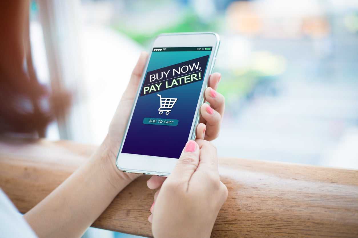 A person holds a smartphone displaying a "Buy Now, Pay Later!" message with a shopping cart icon and an "Add to Cart" button on the screen, reflecting how women are changing their spending behaviors in today’s digital marketplace.