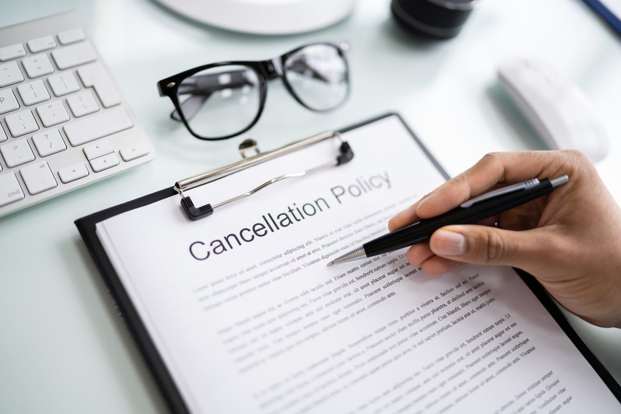 A person holds a pen over a document titled “Cancellation Policy” on a clipboard—an essential consideration for anyone seeking hotel booking tips—with glasses, a keyboard, and a computer mouse nearby.
