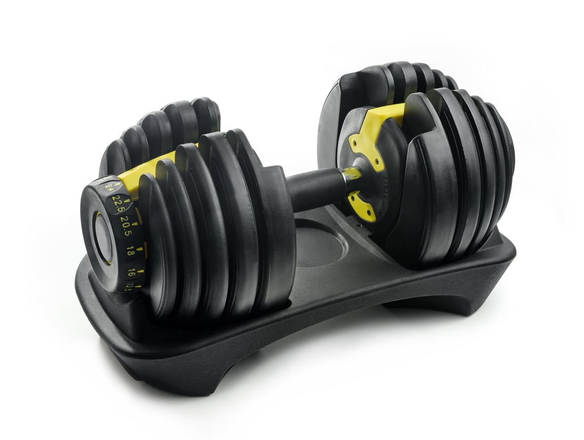 Adjustable dumbbell with black and yellow weight plates, resting on a matching black base, set against a white background. Easily select your desired weight using the side dial and save money by replacing multiple traditional dumbbells.