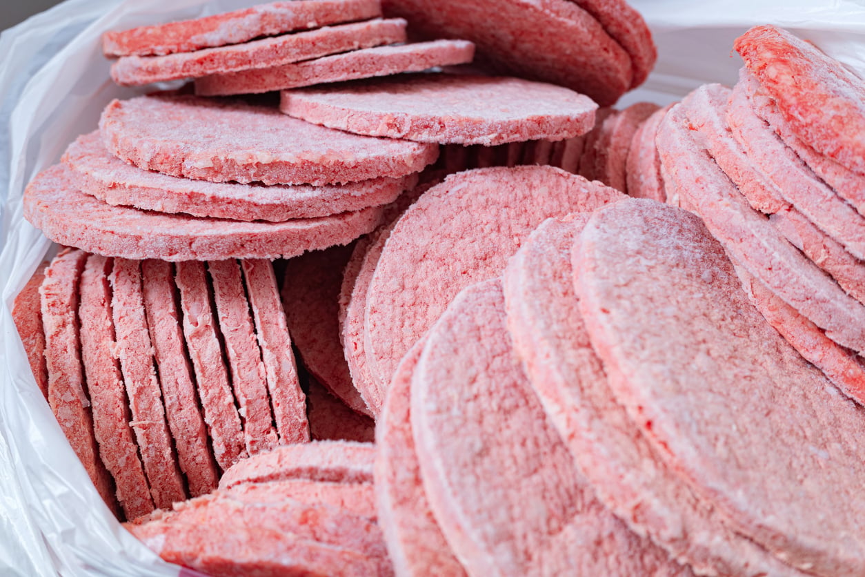 A close-up of a pile of frozen raw hamburger patties stacked together inside a plastic bag.