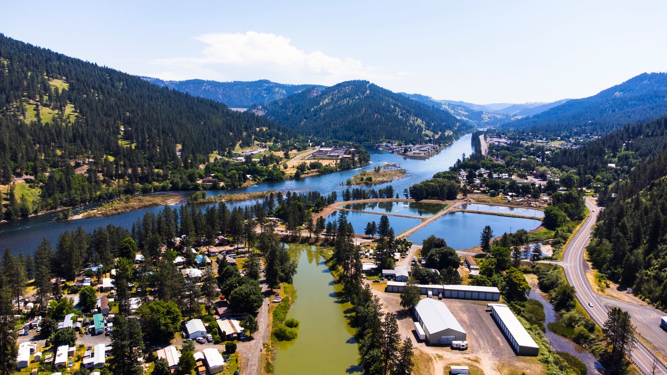 Aerial view of a small town nestled between tree-covered hills, rivers, and ponds, with scattered buildings, roads, and lush greenery under a clear blue sky—one of the 20 travel destinations perfect for exploring picturesque landscapes and hidden gems.