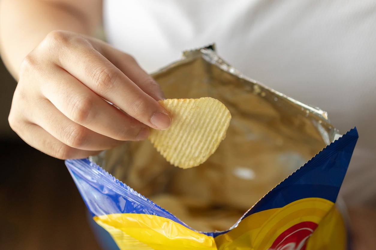 A person holds a ridged potato chip above an open bag of chips, evoking nostalgia for products people no longer buy. The person is wearing a white shirt, and the focus is on their hand and the chip.