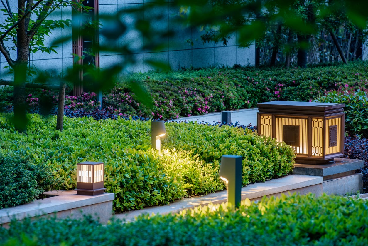 Modern garden path with lush green bushes, illuminated by decorative square lanterns and sleek pathway lights—premium outdoor home products that create a serene outdoor atmosphere during the evening.