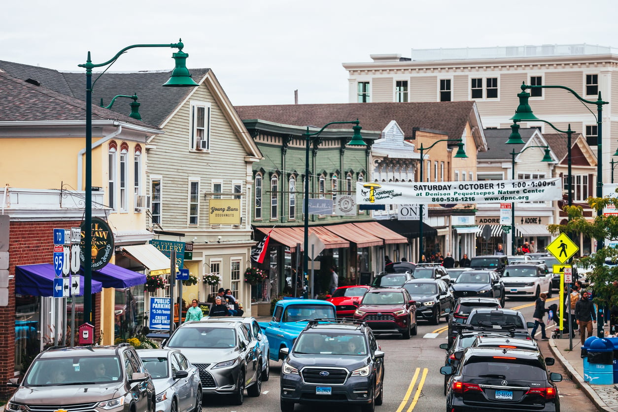 Busy downtown street with cars and people, lined with colorful shops and restaurants; a marquee announces an upcoming event. The scene has a lively, small-town atmosphere under an overcast skyāfar removed from the home features homeowners no longer want, embracing instead the vibrant charm that modern communities seek.