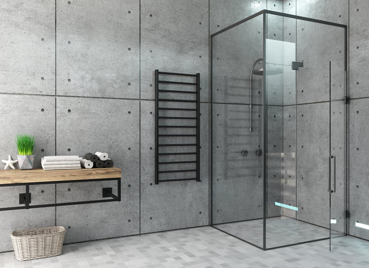 A modern bathroom with concrete walls, a glass shower enclosure, a wall-mounted towel rack, and a wooden countertop with towels and decor—perfect for showcasing recent hotel changes—plus a basket on the tiled floor.