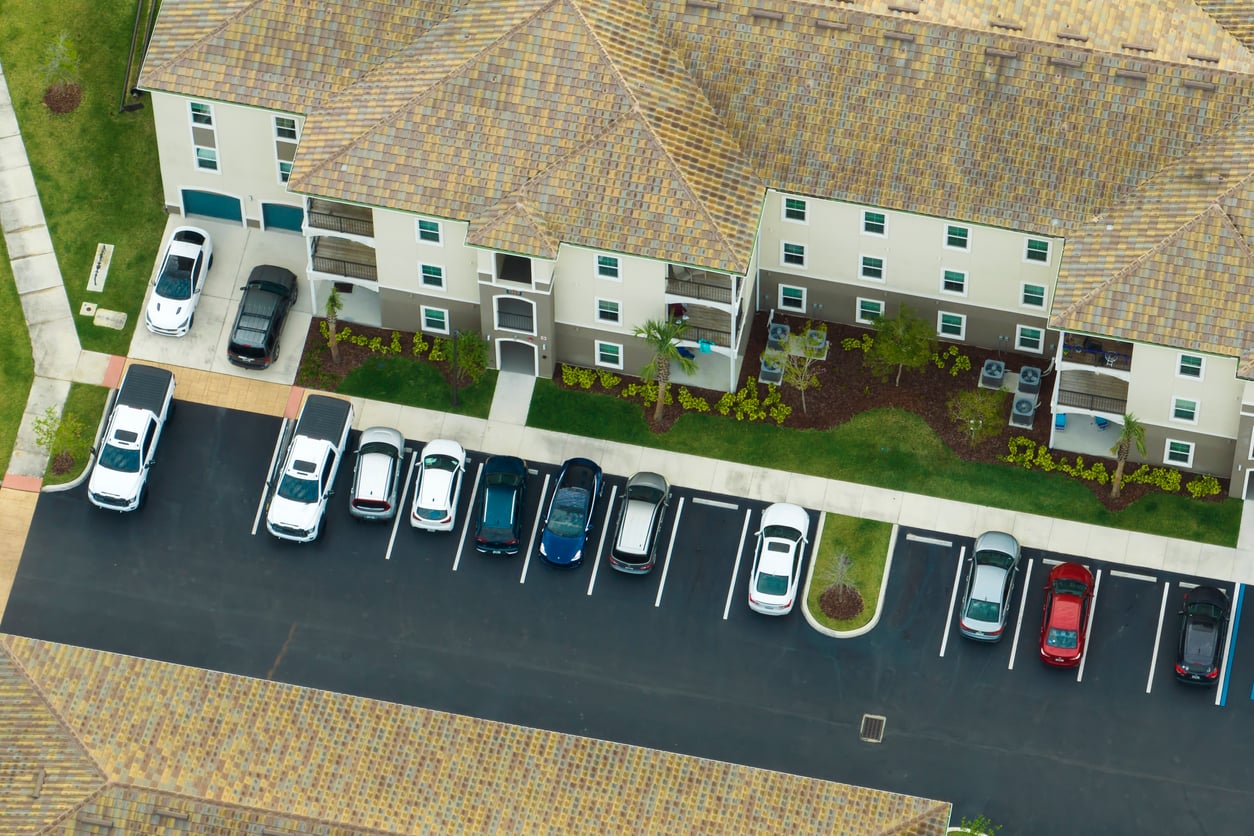 Aerial view of an apartment complex with parked cars in a lot next to beige buildings with tiled roofs, green grass, and landscaping—a scene that rivals many vacation spots discovered using expert hotel booking tips.