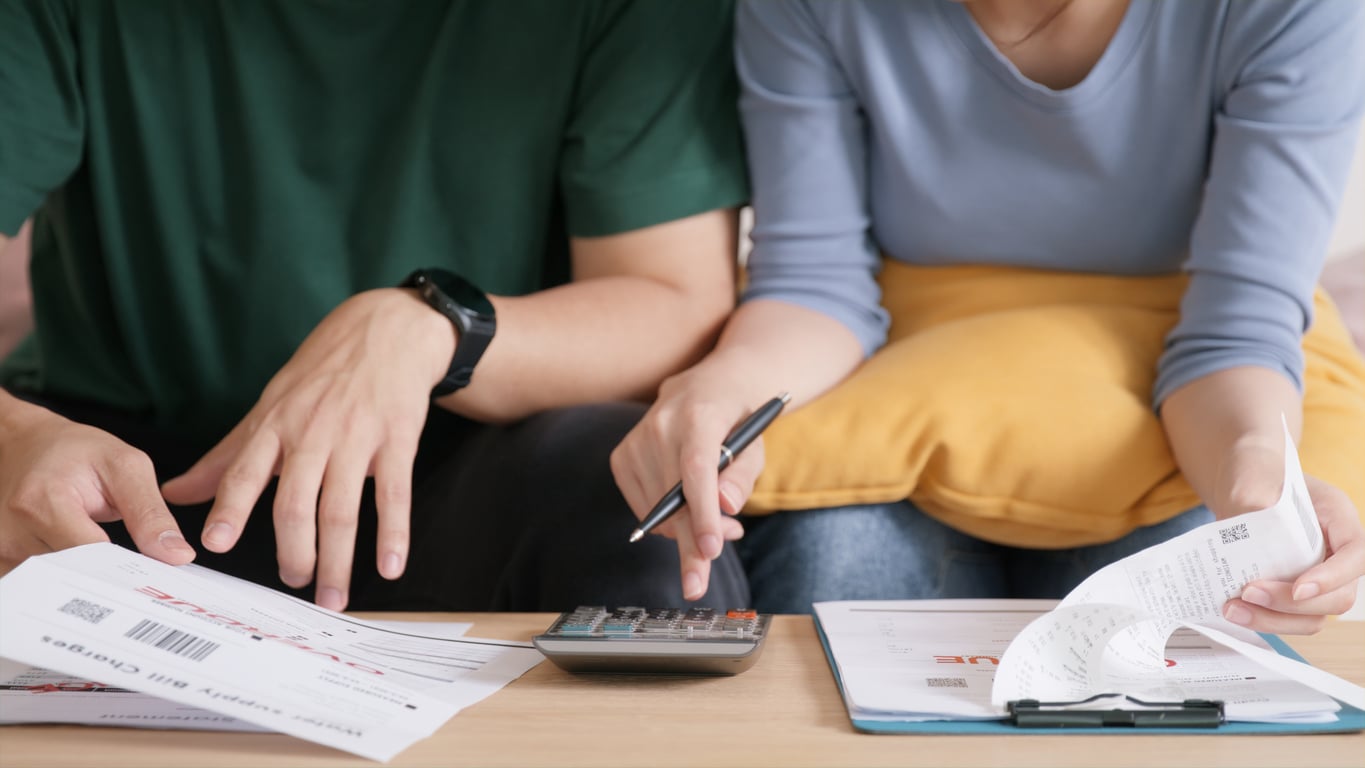 Two people sitting at a table, using a calculator and reviewing bills, receipts, and documents, suggesting they are budgeting together and discussing the benefits of renting.
