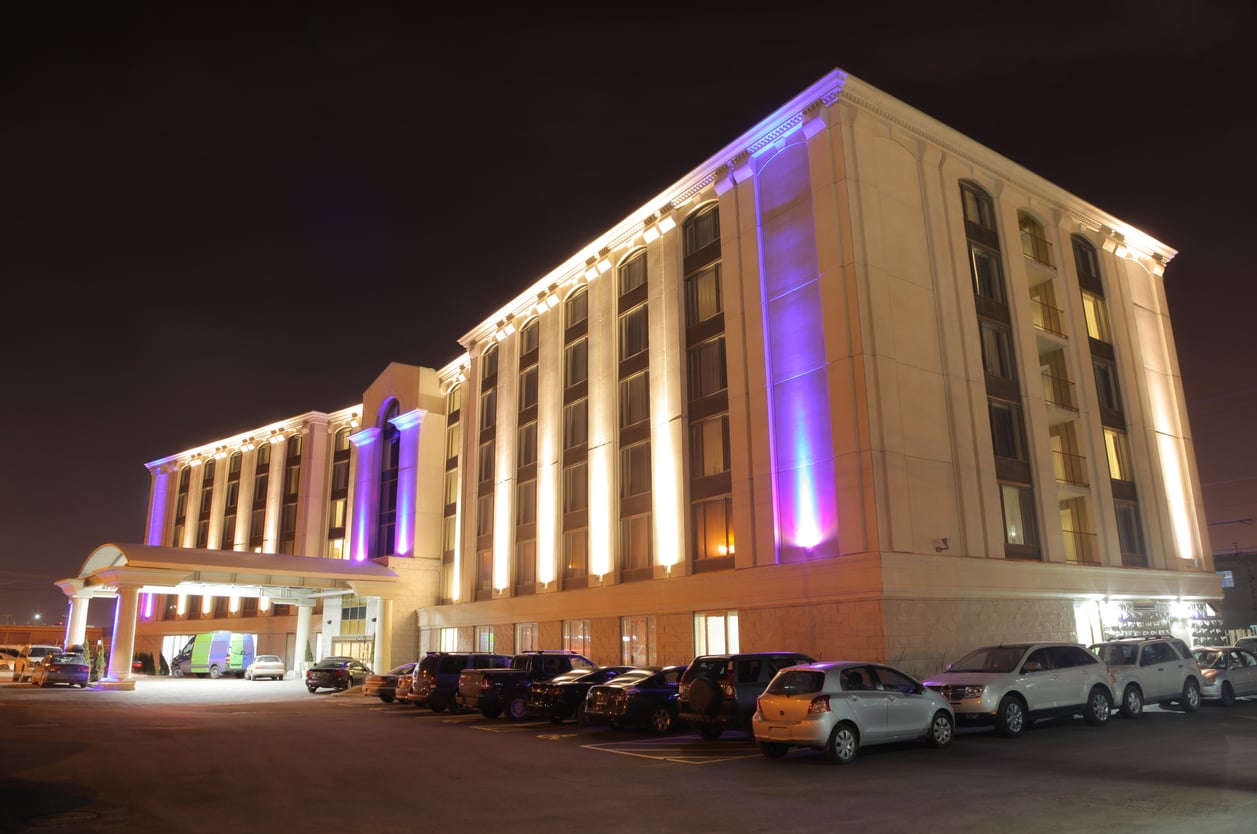 A large, modern hotel building at night with glowing white and purple lights, multiple windows, and a parking lot filled with cars in front—reminding travelers to avoid common hotel booking mistakes for a stress-free stay.
