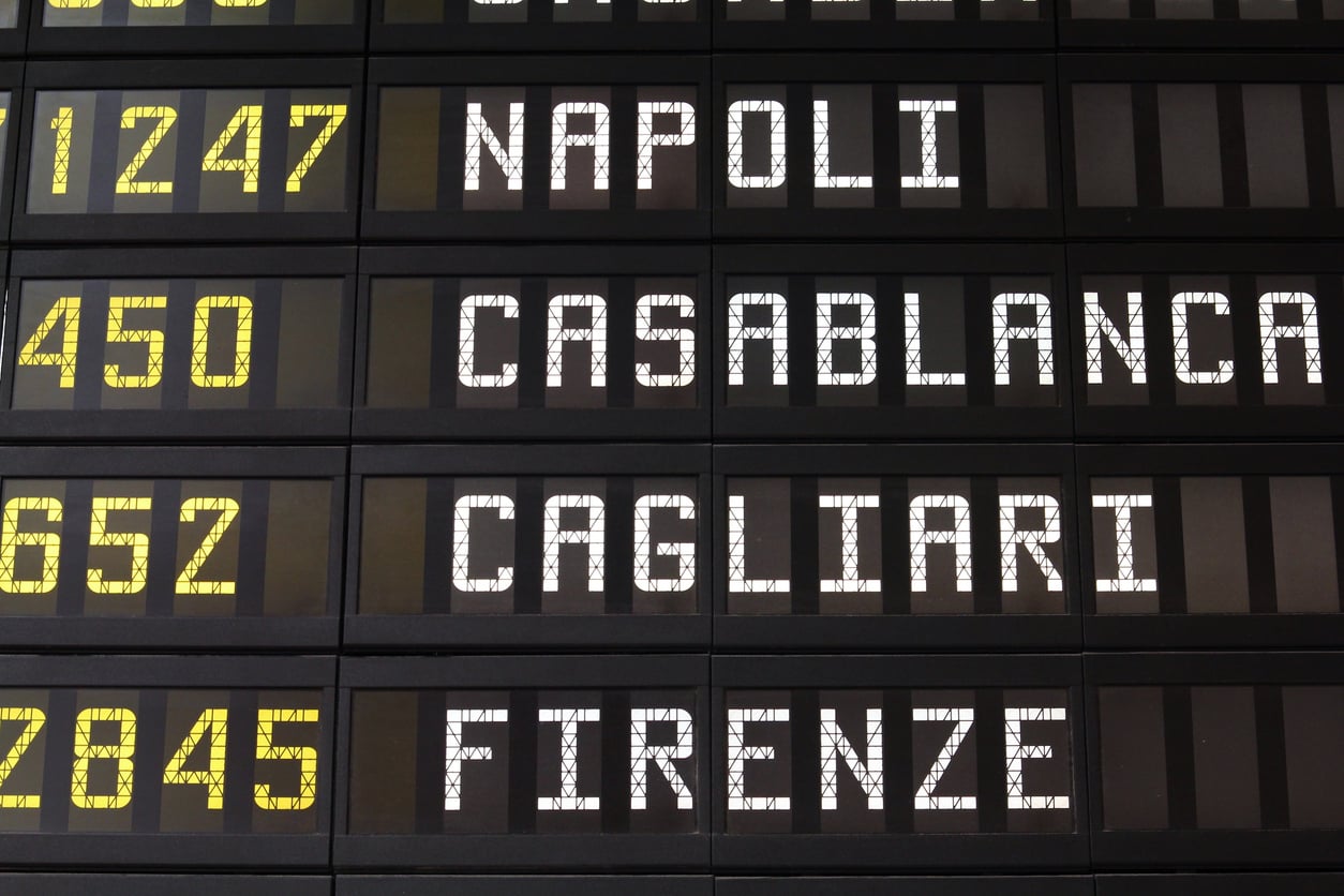 Close-up of an airport departure board showing flight numbers and destinations: Napoli, Casablanca, Cagliari, and Firenze.