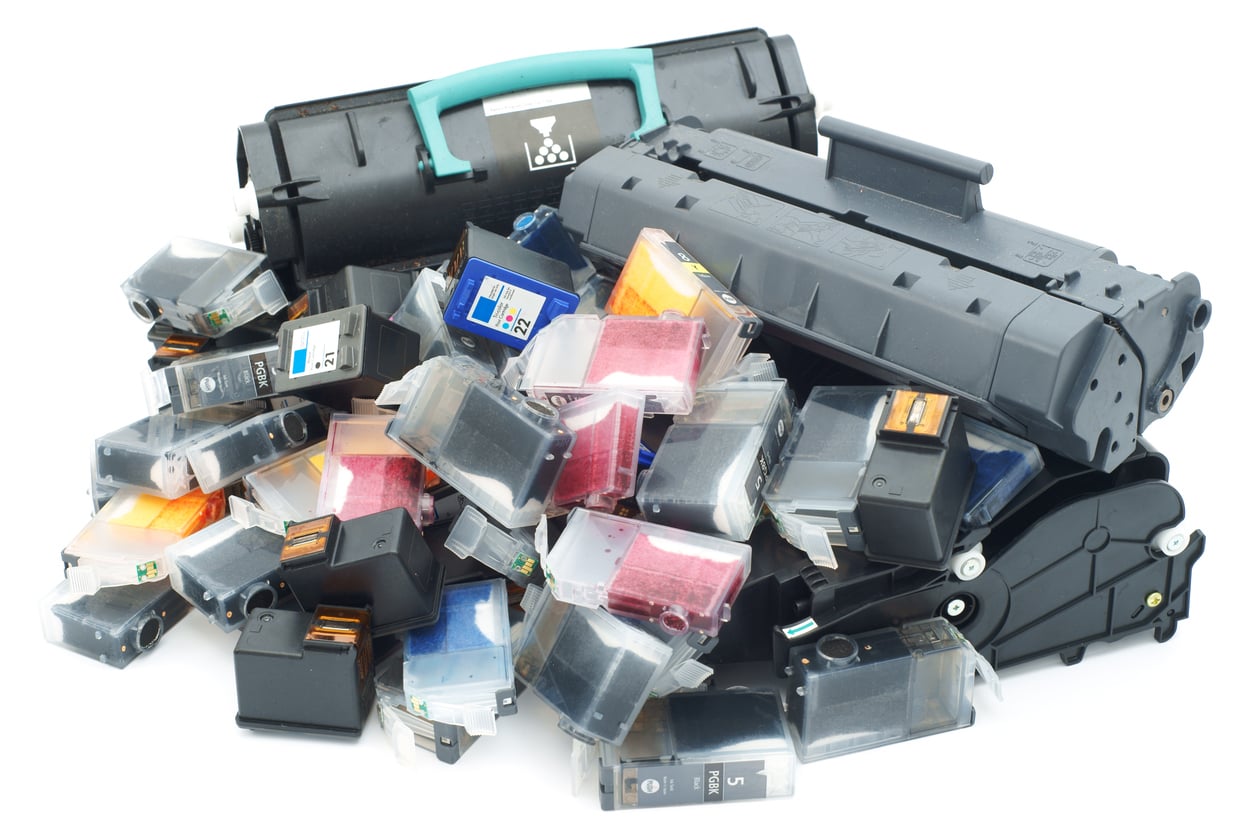 A pile of used printer ink cartridges and two large toner cartridges from Walmart are displayed on a white background, showing a mix of colors and sizes, with some cartridges slightly stained with ink.