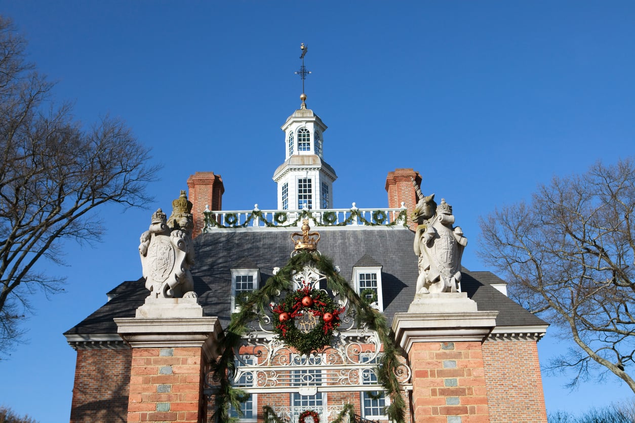 Set in one of the best Christmas towns in America, this colonial-style brick building features statues, holiday wreaths, and garlands adorning the gate, all beautifully framed by bare trees beneath a clear blue sky.