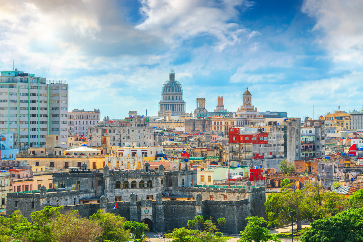 Colorful cityscape of Havana, Cuba, featuring the Capitolio building, historic architecture, and vibrant buildings under a bright blue sky with clouds—an iconic scene among renowned travel destinations.