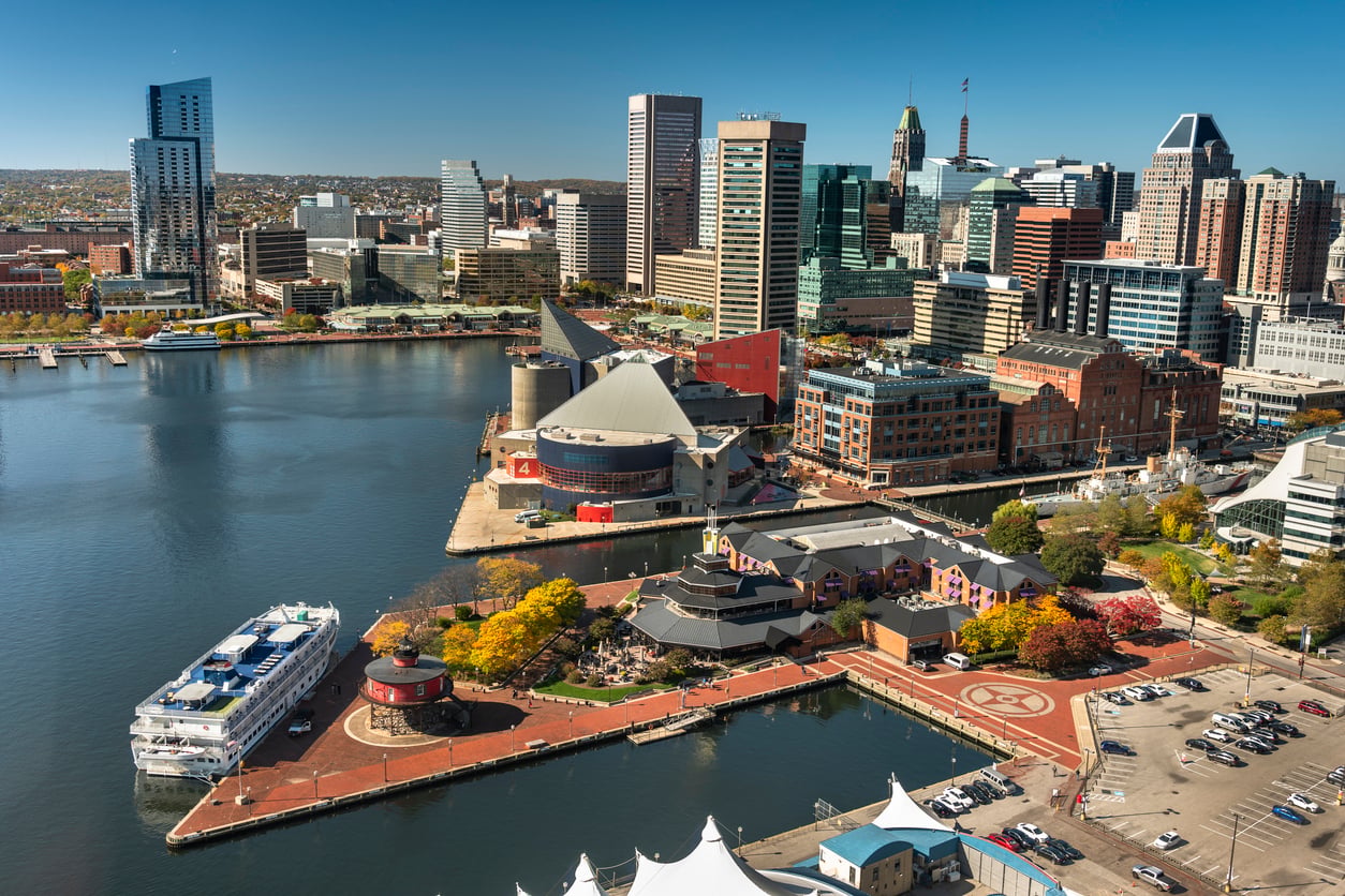 Aerial view of Baltimore Inner Harbor—one of the top 20 travel destinations—showcasing boats docked, modern high-rise buildings, and waterfront attractions under a clear blue sky.