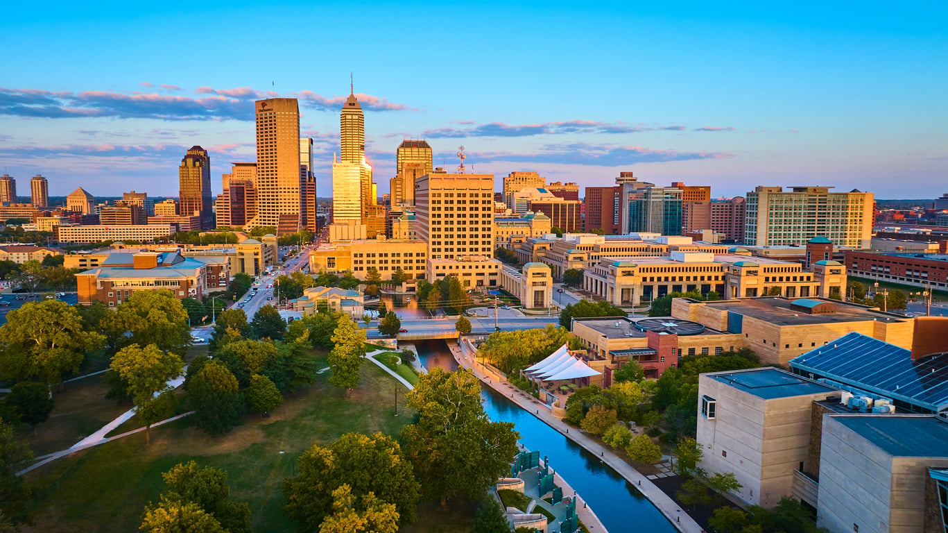 Aerial view of downtown Indianapolis at sunset, showing tall buildings, green parks, and a canal running through the city under a clear sky—one of the top 20 travel destinations for urban explorers seeking vibrant cityscapes and scenic beauty.