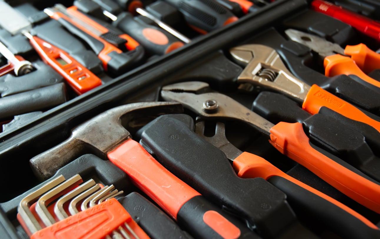 A close-up of a tool kit containing durable hand tools—unlike products that don't last—such as a hammer, pliers, wrenches, screwdrivers, and hex keys, all organized in a black and orange foam case.