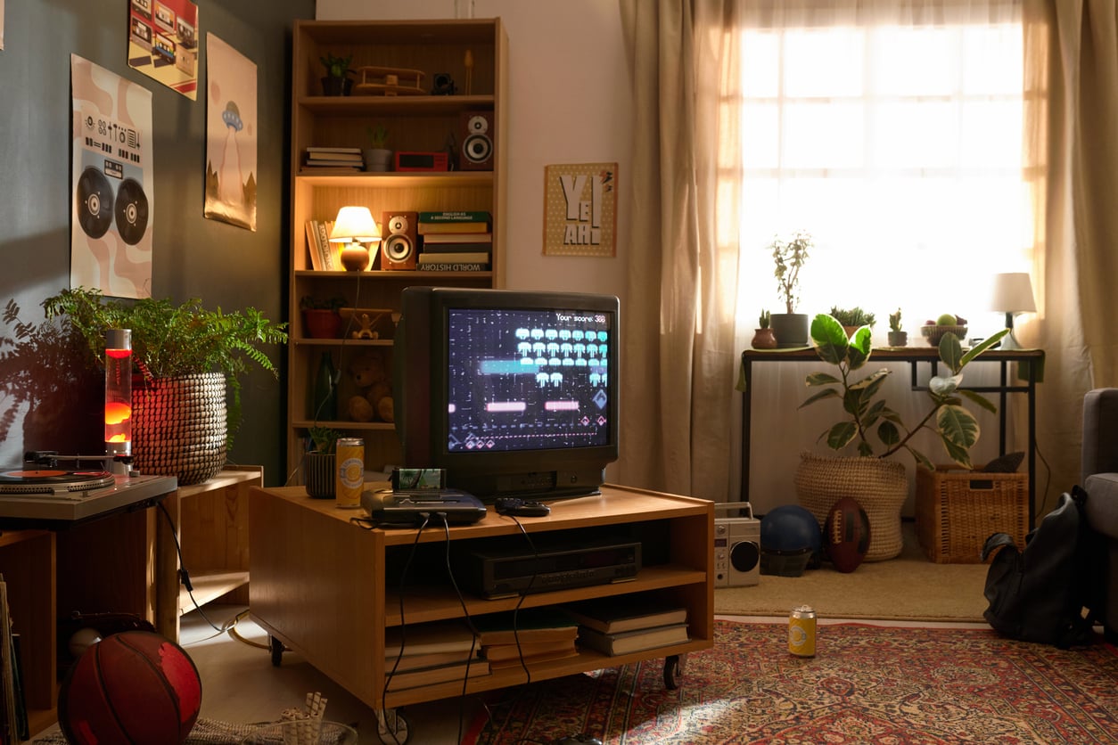A cozy living room reminiscent of Middle-Class Moms in the 80s and 90s, with plants, bookshelves, and a retro TV displaying a video game. Sunlight filters through the curtains, casting a warm glow on various items like books, a basketball, and a rug scattered around the room.
