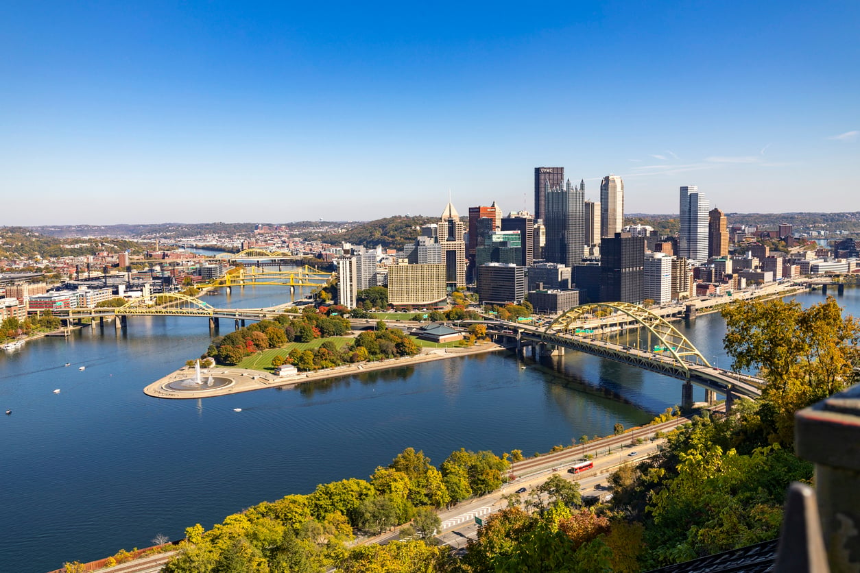 Aerial view of downtown Pittsburgh, one of the notable big cities in America, showing skyscrapers, rivers, bridges, and Point State Park with the fountain on a clear, sunny day.