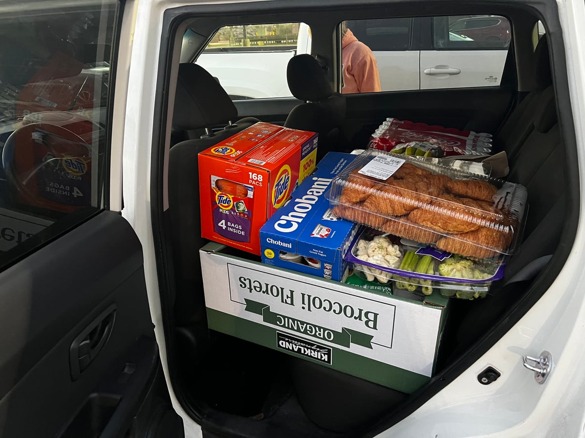 A car’s backseat loaded with groceries—evidence of thoughtful grocery shopping habits—including a box of Tide Pods, Chobani yogurt, rotisserie chickens, eggs, and a box labeled “Organic Broccoli Florets.”