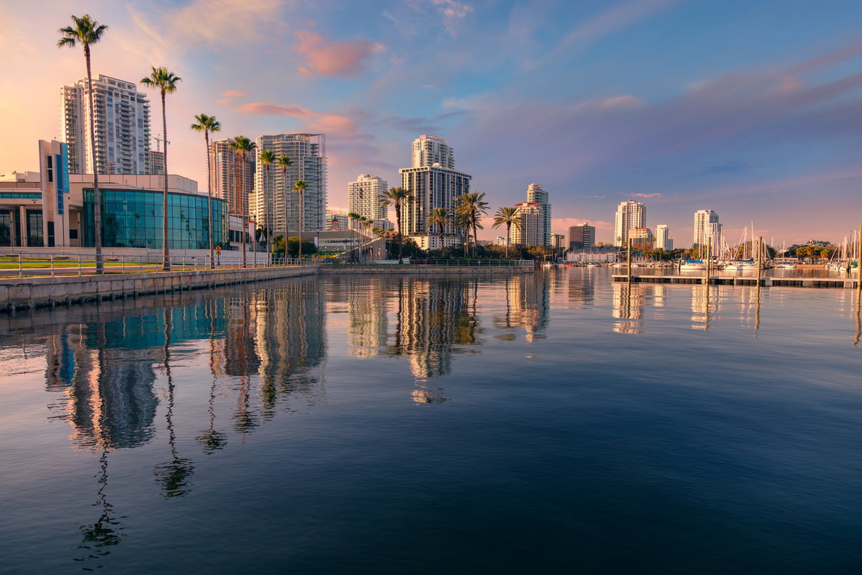 A calm waterfront scene at sunset with tall buildings, palm trees, and boats reflected in the water under a colorful sky evokes the allure of top 20 travel destinations around the world.